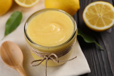 Photo of Delicious lemon curd in bowl, fresh citrus fruits and spoon on wooden table, closeup