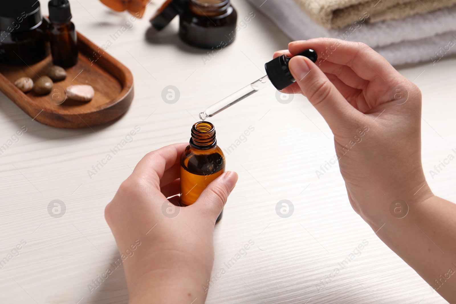 Photo of Woman with bottle of cosmetic serum and pipette at white wooden table, closeup