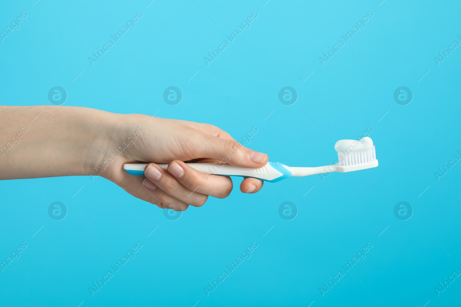 Photo of Woman holding toothbrush with paste on light blue background, closeup