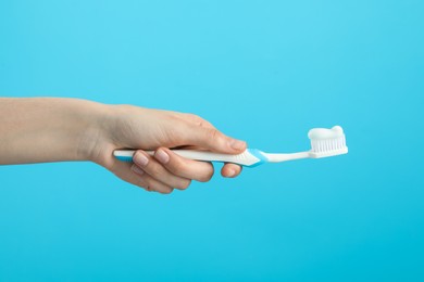 Woman holding toothbrush with paste on light blue background, closeup