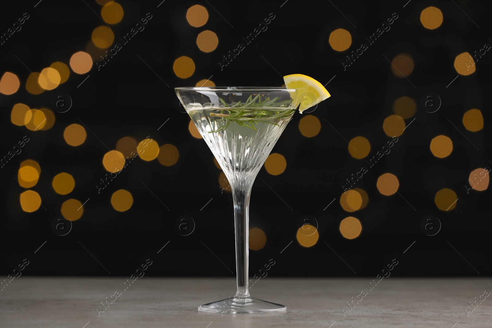 Photo of Martini glass of refreshing cocktail with lemon slice and rosemary on light grey table