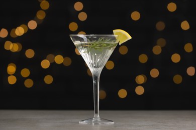 Martini glass of refreshing cocktail with lemon slice and rosemary on light grey table