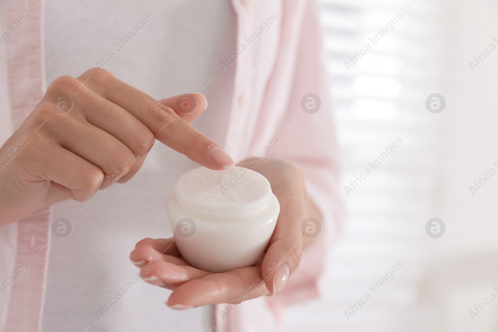 Photo of Woman holding jar with cream near window, closeup
