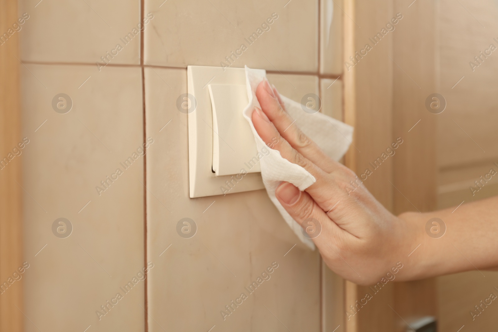 Photo of Woman cleaning light switch with napkin indoors, closeup