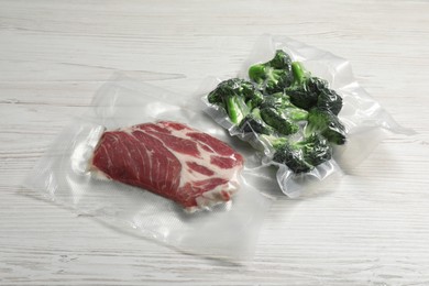 Photo of Raw beef and broccoli in vacuum packs on white wooden table