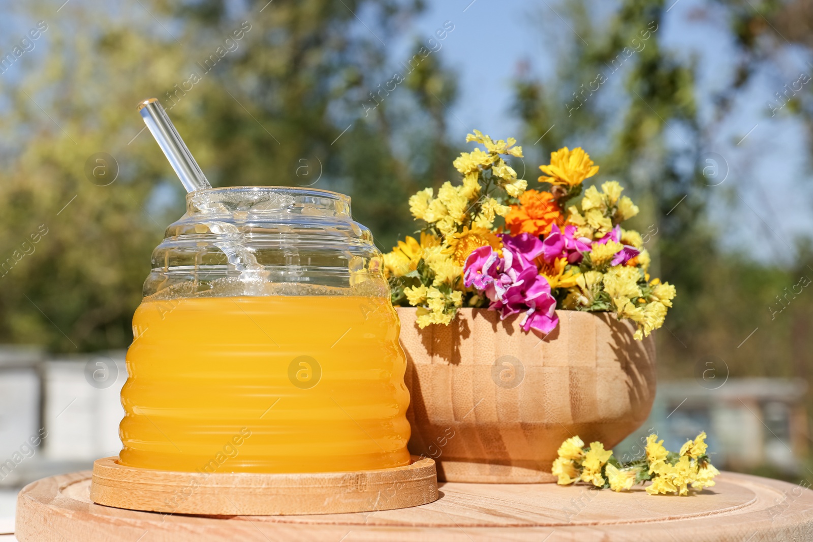 Photo of Delicious fresh honey and beautiful flowers on wooden board in apiary