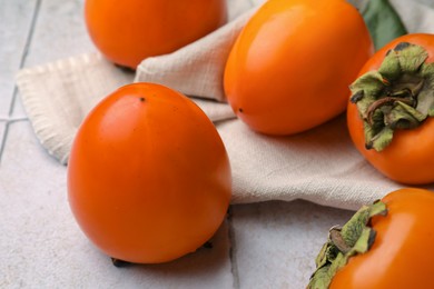 Photo of Delicious ripe juicy persimmons on tiled surface, closeup