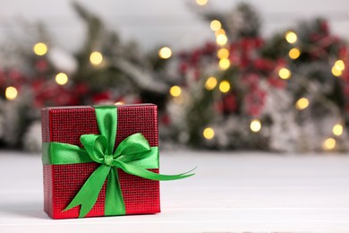 Photo of Beautiful gift box on white table against blurred festive lights, space for text. Christmas present