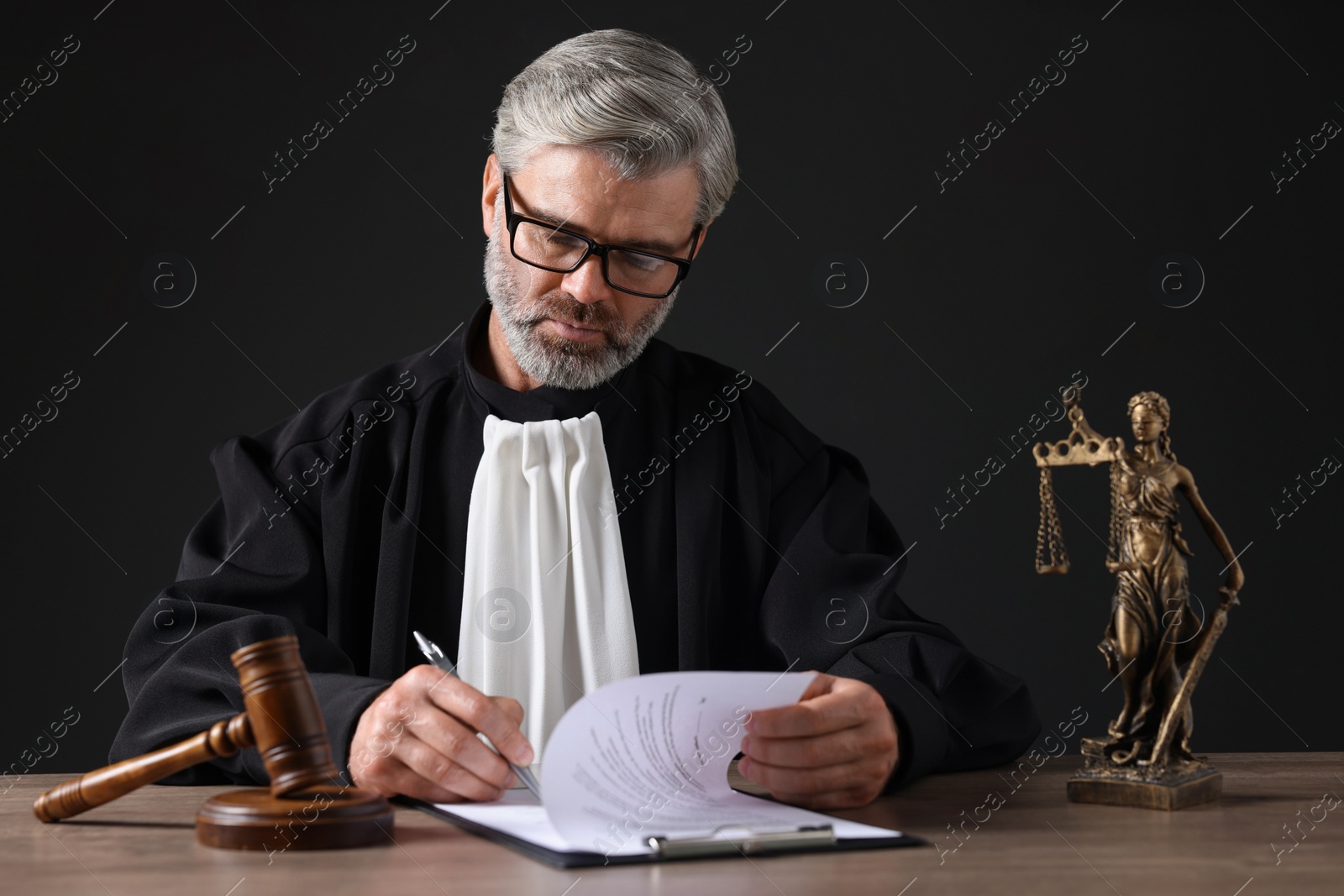 Photo of Judge working with documents at wooden table against black background