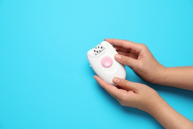 Woman holding modern epilator on light blue background, top view. Space for text