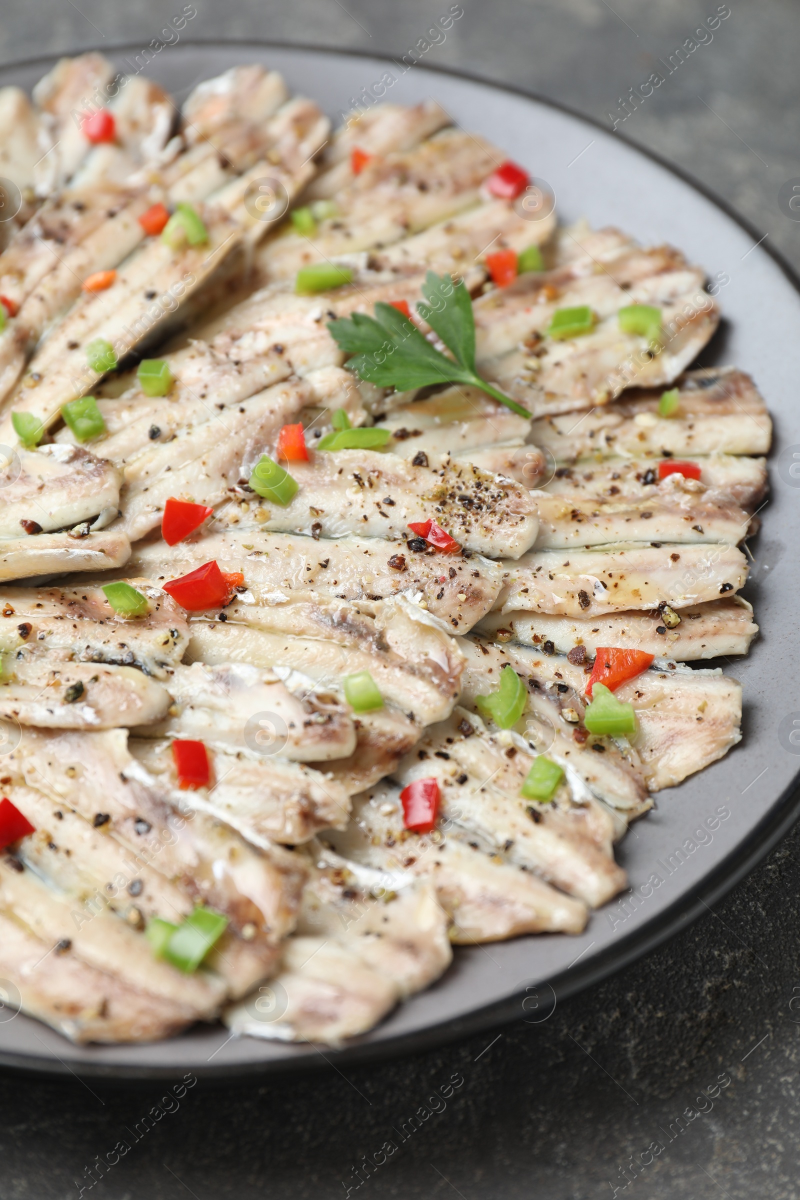 Photo of Tasty pickled anchovies with spices on grey textured table, closeup