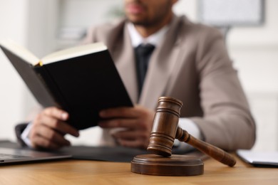 Lawyer reading book at table in office, focus on gavel