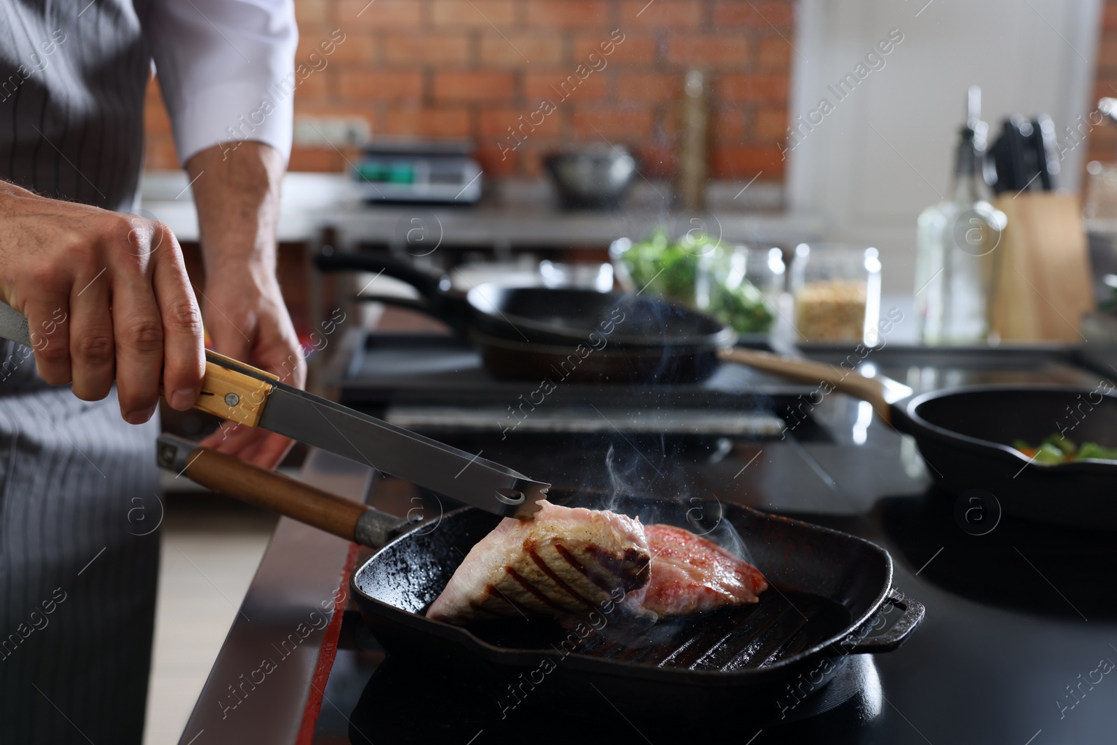 Photo of Professional chef cooking meat on stove in restaurant kitchen, closeup