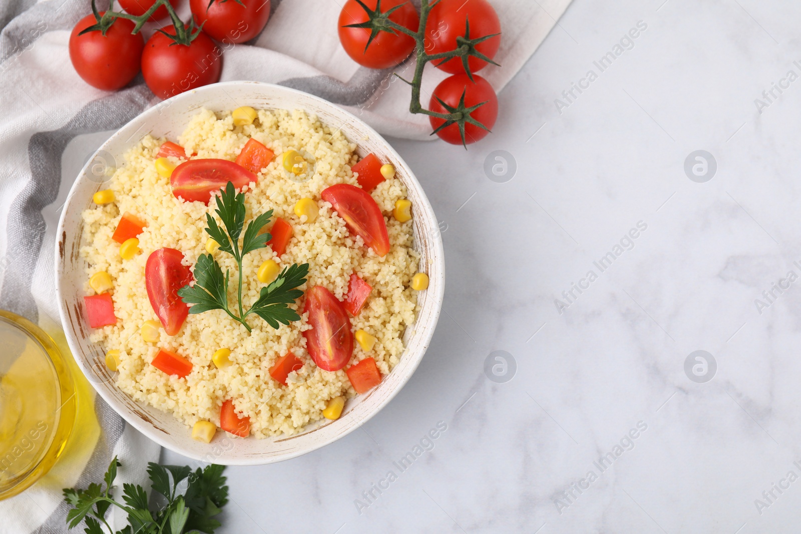 Photo of Tasty couscous with parsley, corn and tomatoes served on white marble table, flat lay. Space for text