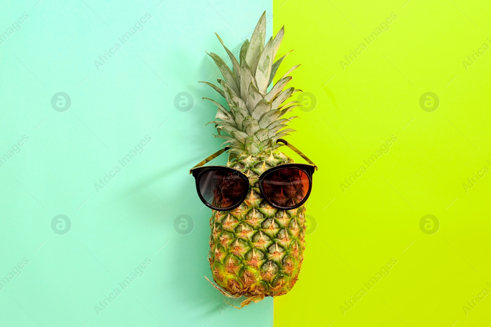 Photo of Fresh ripe pineapple with sunglasses on color background, top view