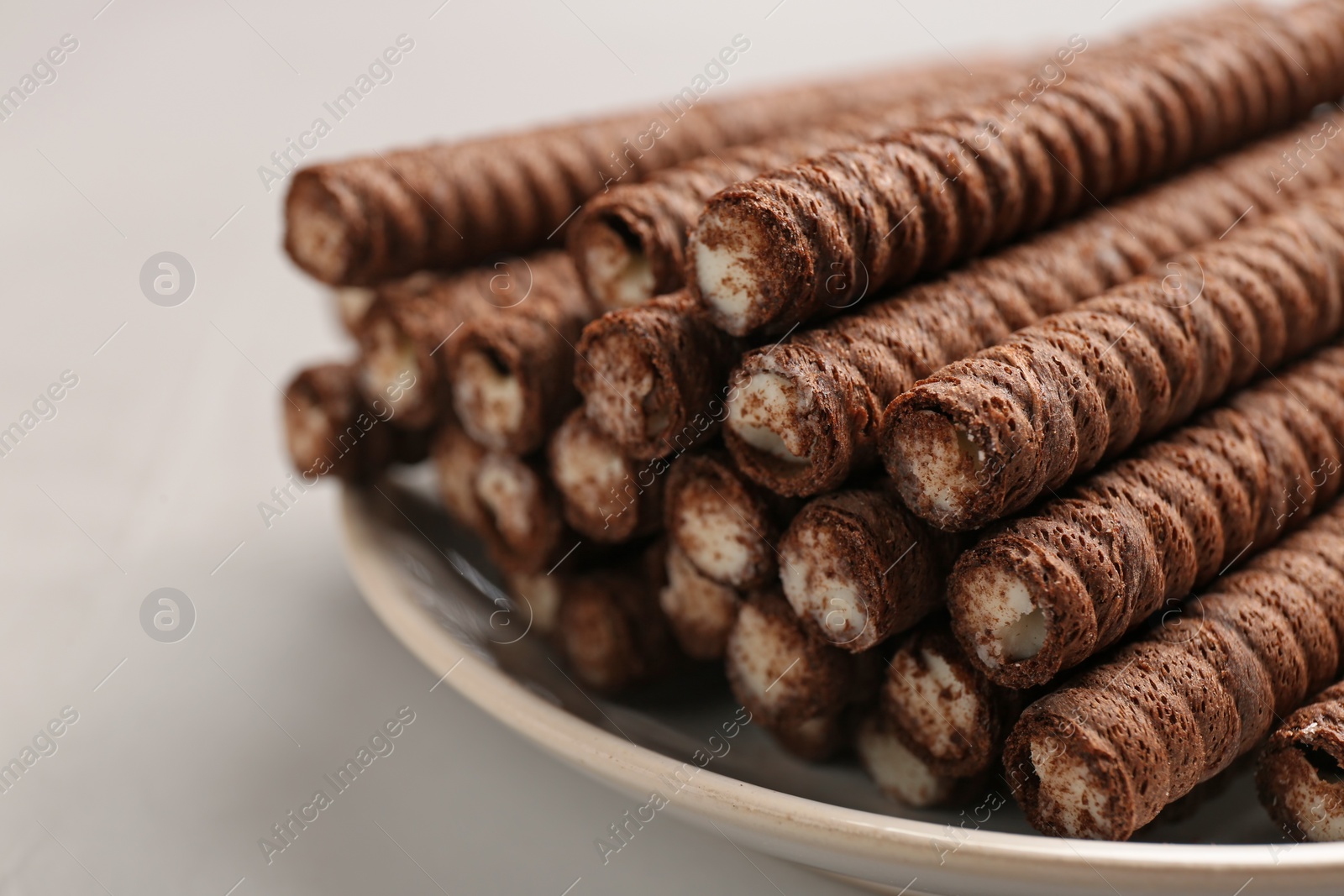 Photo of Plate with delicious chocolate wafer rolls on white table, closeup. Sweet food