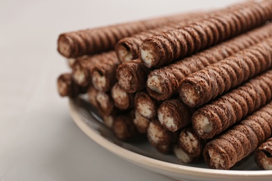 Plate with delicious chocolate wafer rolls on white table, closeup. Sweet food