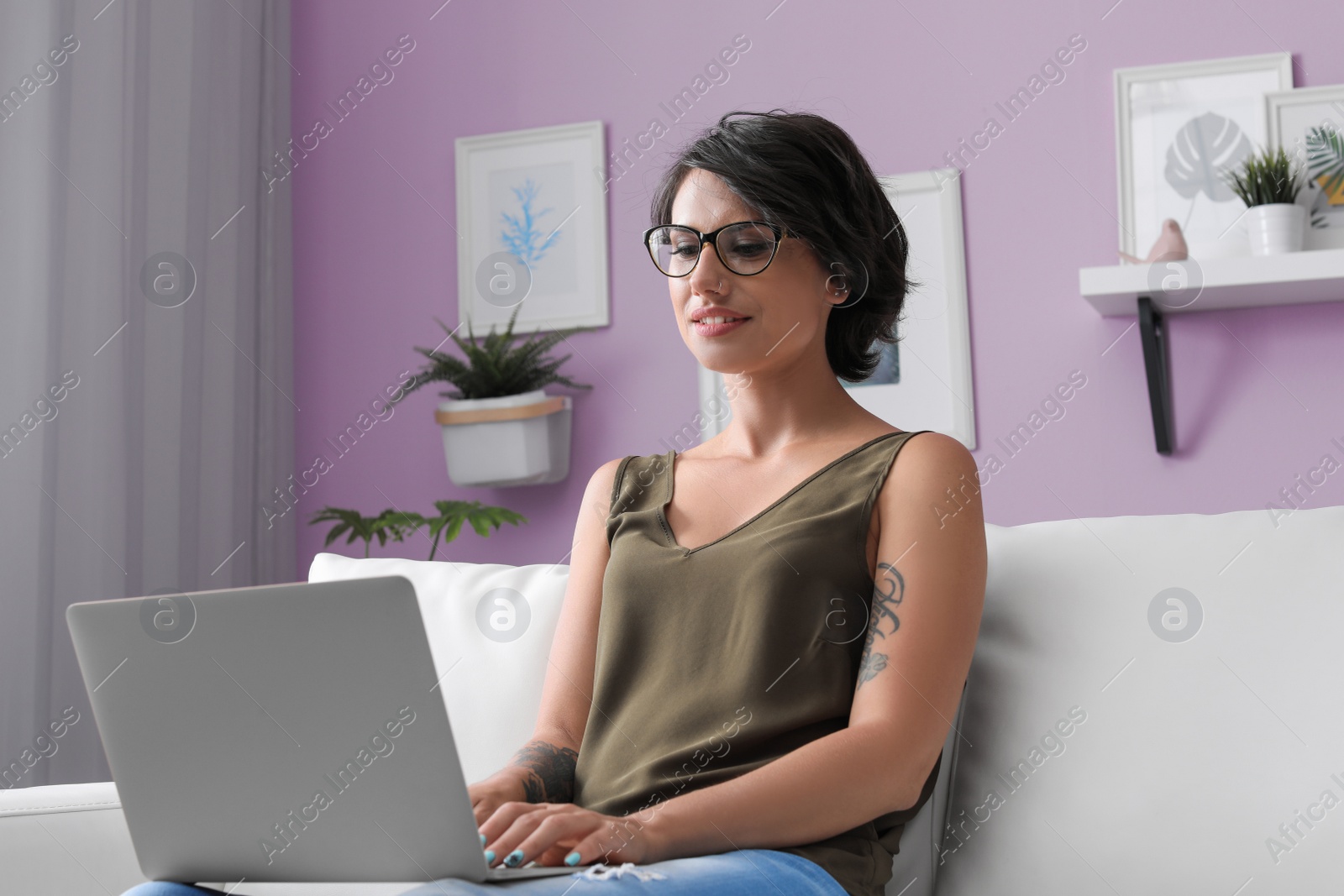 Photo of Young woman with modern laptop sitting on sofa at home