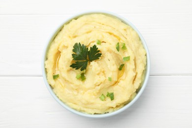 Photo of Bowl of tasty mashed potatoes with parsley and green onion on white wooden table, top view