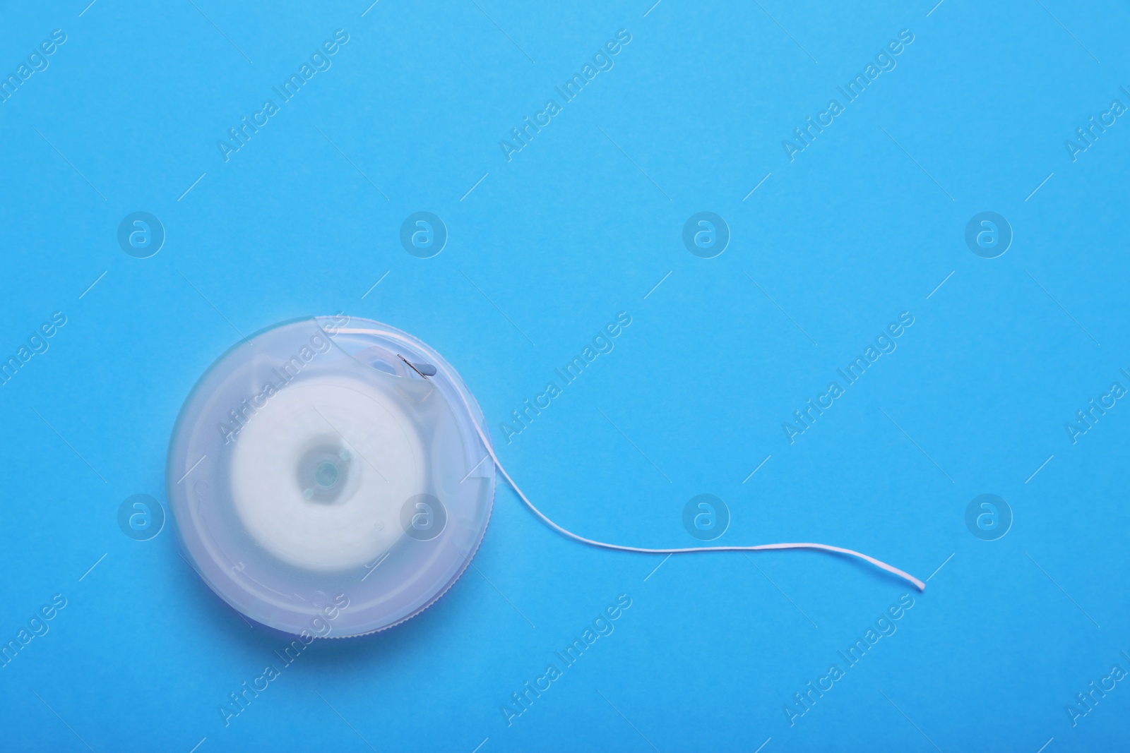 Photo of Container with dental floss on light blue background, top view. Space for text