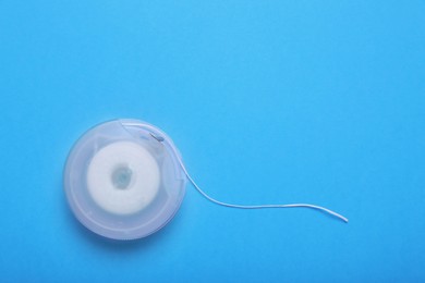 Container with dental floss on light blue background, top view. Space for text