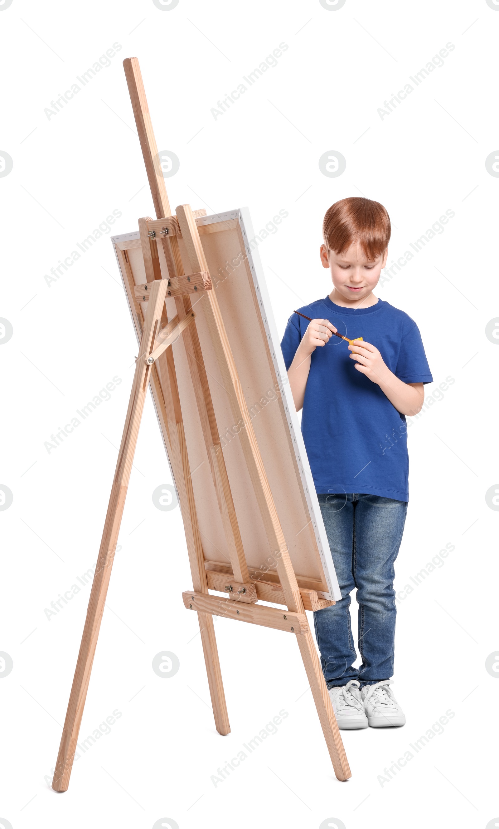 Photo of Little boy painting against white background. Using easel to hold canvas