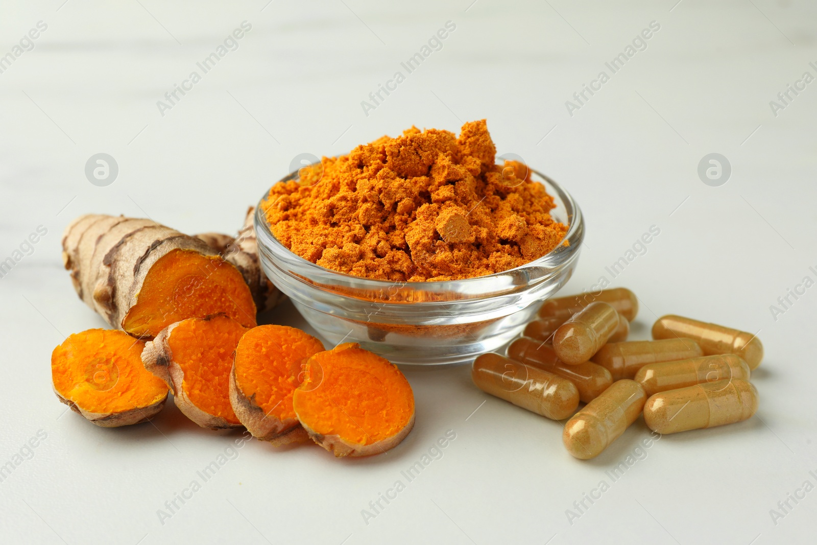 Photo of Aromatic turmeric powder, pills and raw root on white marble table, closeup