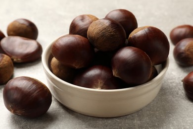 Photo of Bowl with roasted edible sweet chestnuts on light grey table, closeup
