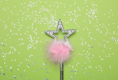 Photo of Beautiful silver magic wand with feather and confetti on light green background, flat lay