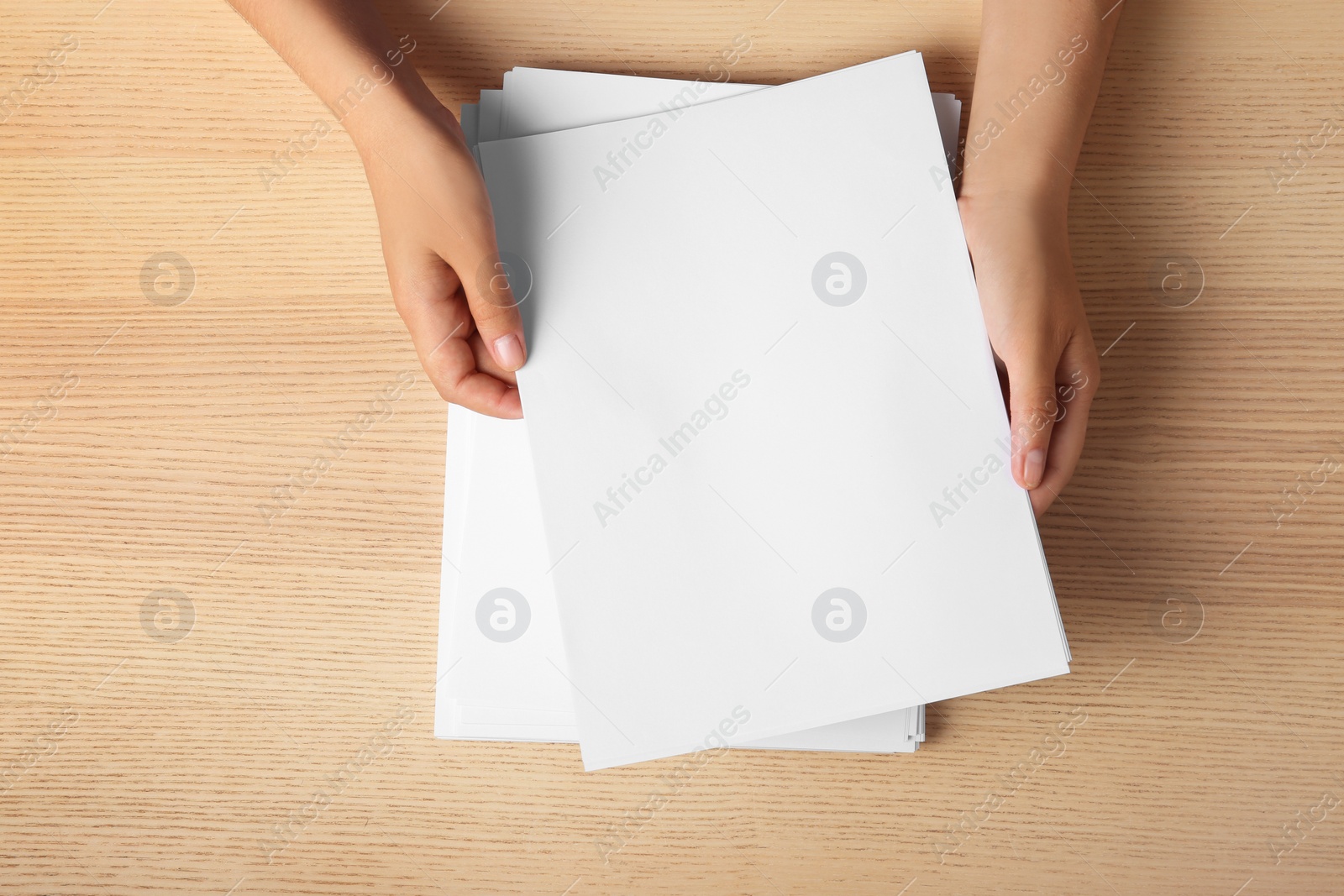 Photo of Woman holding blank paper sheets for brochure at wooden table, top view. Mock up