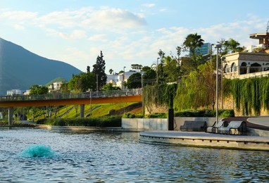 Photo of Picturesque view of park with river, bridge and wooden benches