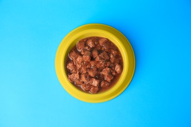 Photo of Wet pet food in feeding bowl on light blue background, top view