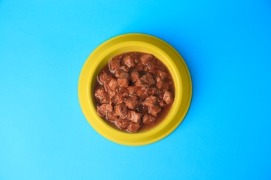 Wet pet food in feeding bowl on light blue background, top view