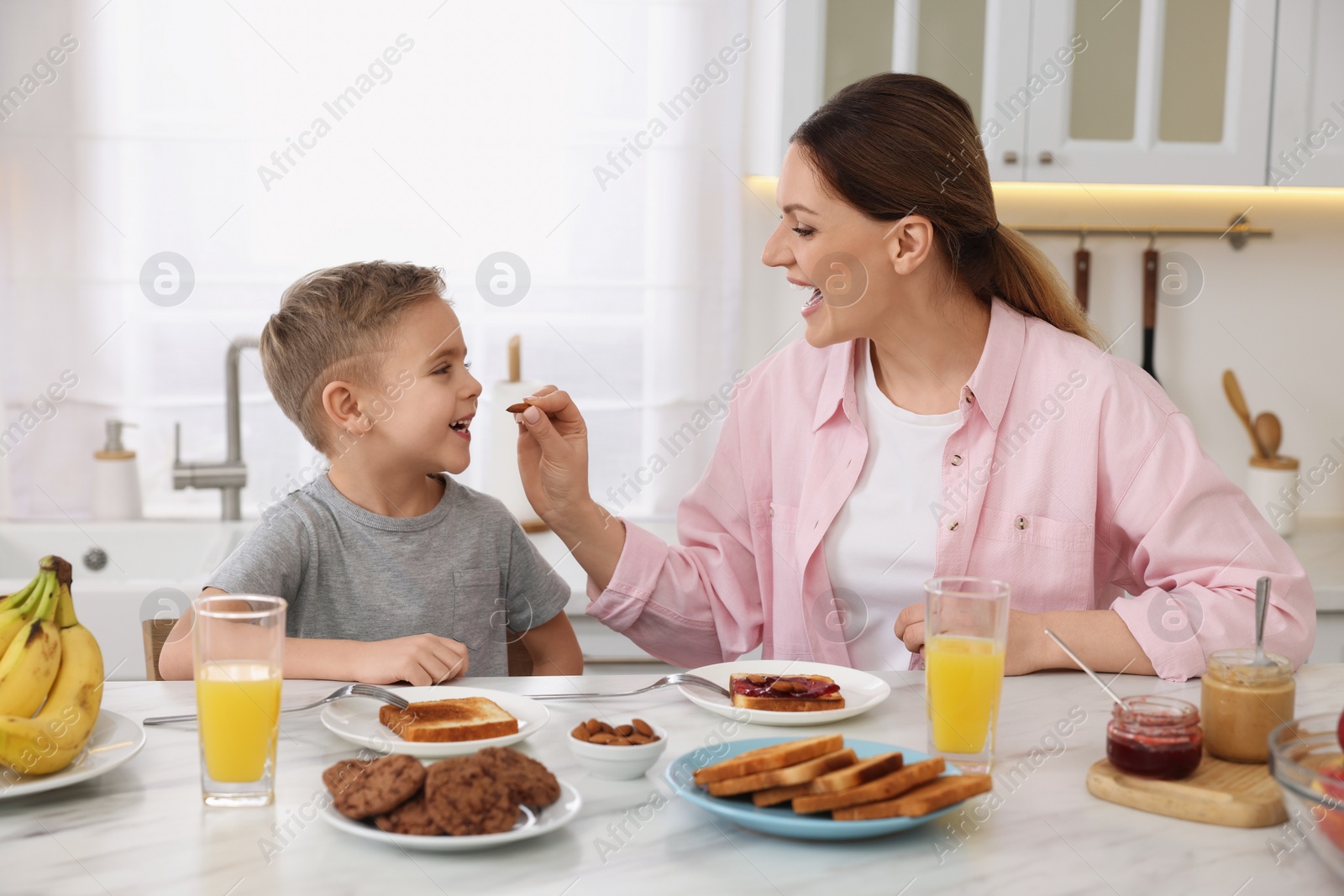 Photo of Mother and her cute little son having breakfast at table in kitchen