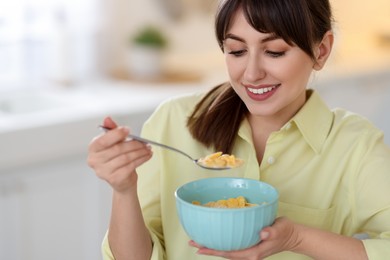 Smiling woman eating tasty cornflakes at breakfast indoors