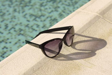 Stylish sunglasses near outdoor swimming pool on sunny day