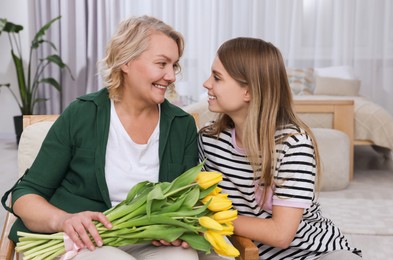 Photo of Young daughter congratulating her mom with flowers at home. Happy Mother's Day