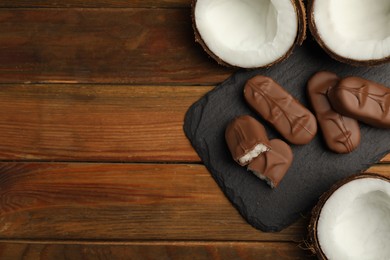 Photo of Delicious milk chocolate candy bars with coconut filling on wooden table, flat lay. Space for text