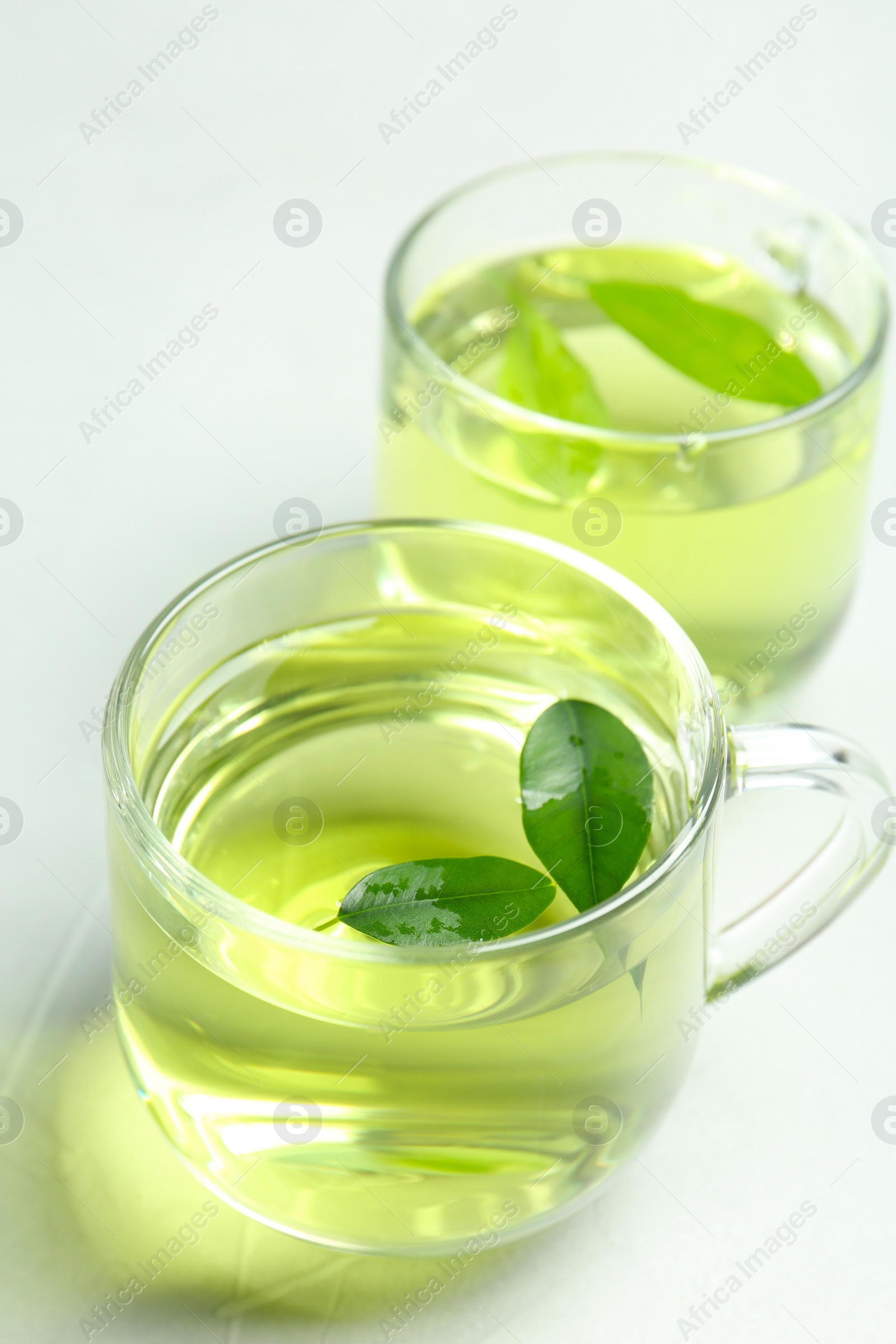 Photo of Cups of aromatic green tea on light table