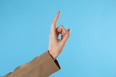Businesswoman pointing at something on light blue background, closeup. Finger gesture
