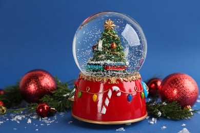 Photo of Beautiful snow globe, Christmas balls and coniferous twigs on blue background