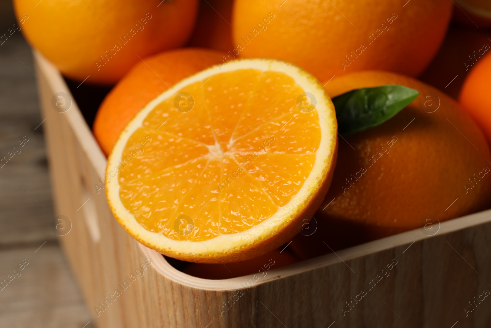 Photo of Many whole and cut ripe oranges on wooden table, closeup