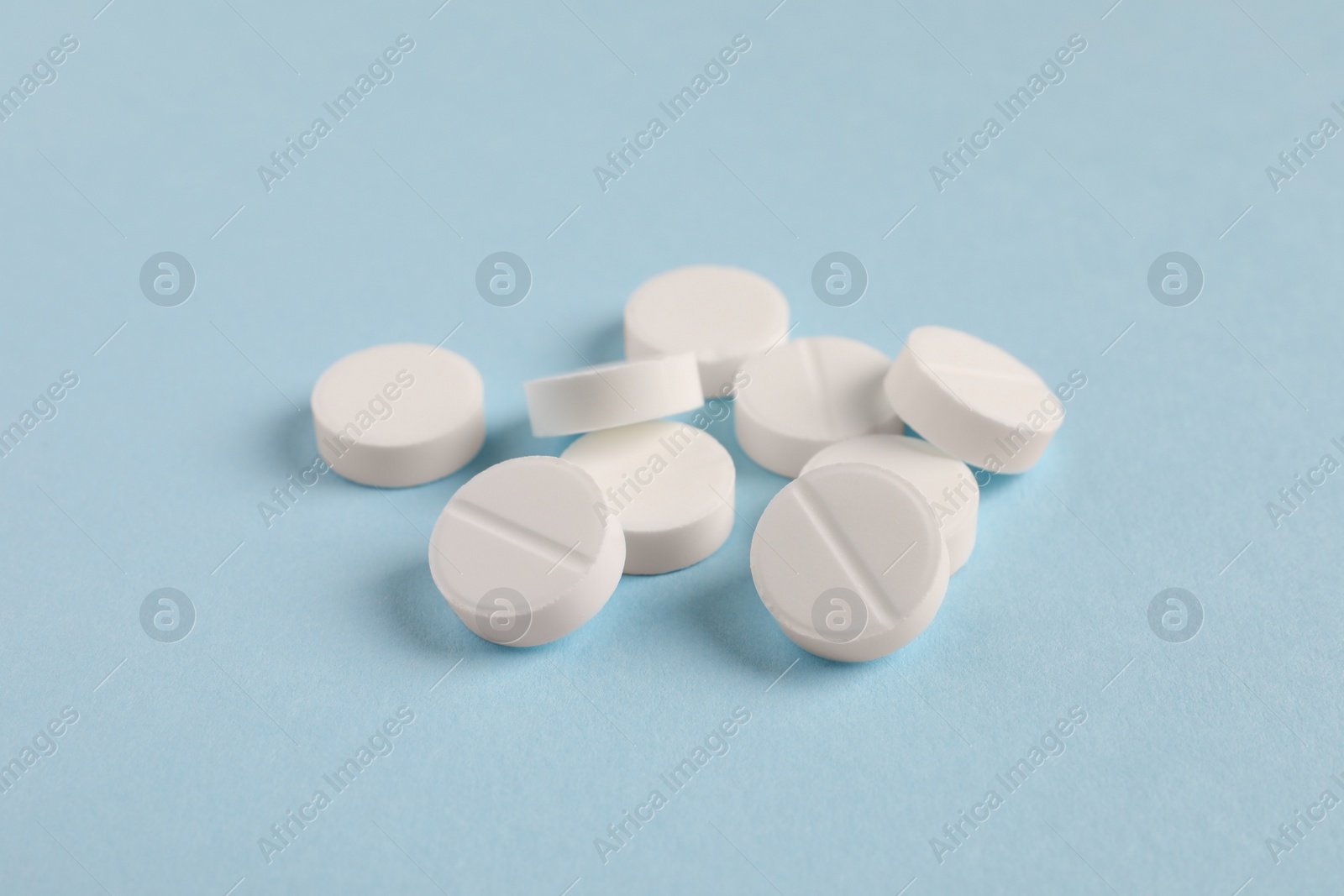 Photo of Pile of white pills on light blue background, closeup