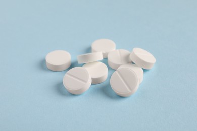 Pile of white pills on light blue background, closeup