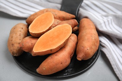 Photo of Slate board with cut and whole sweet potatoes on light grey table, closeup
