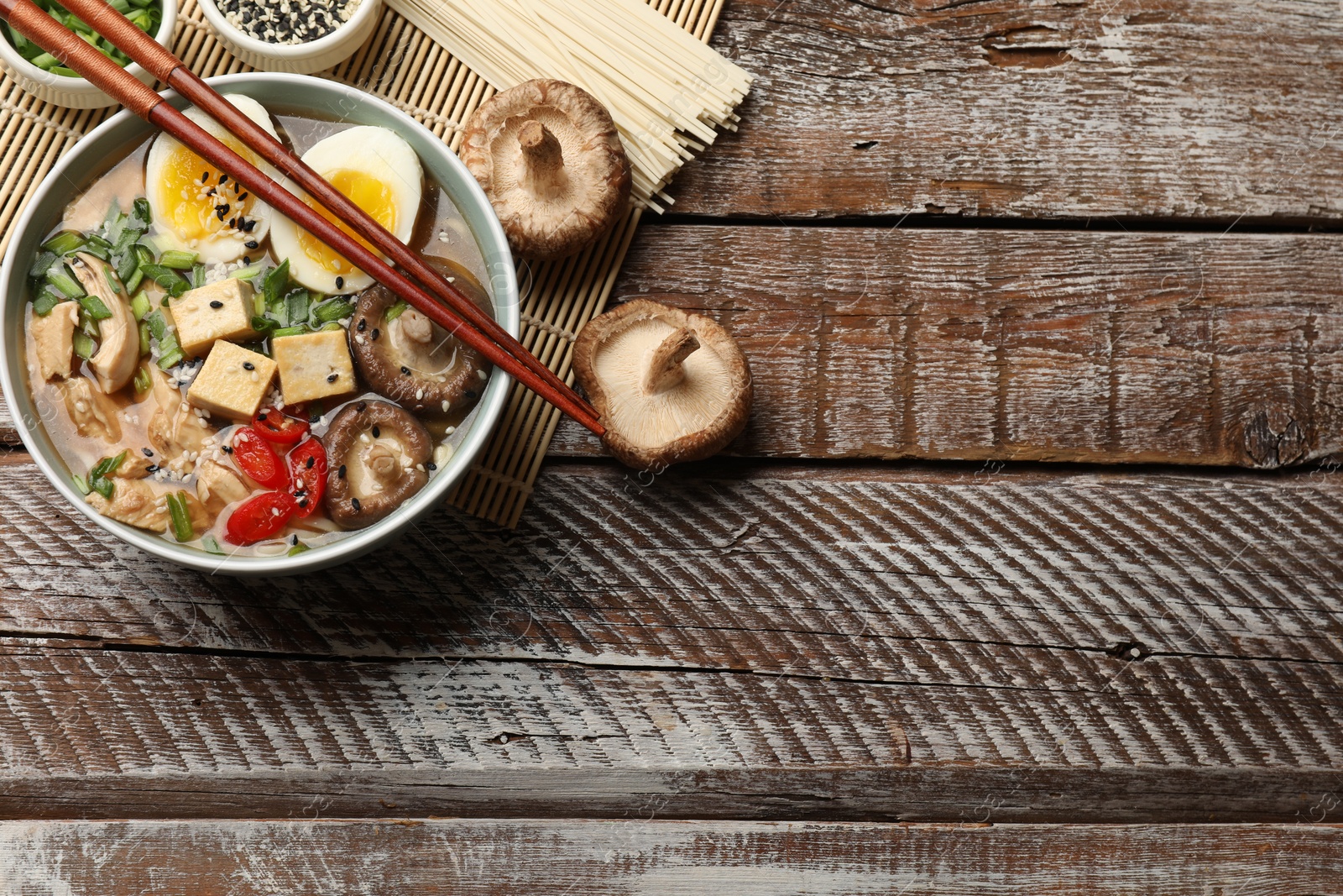 Photo of Noodle soup. Bowl of delicious ramen and chopsticks on wooden table, flat lay. Space for text