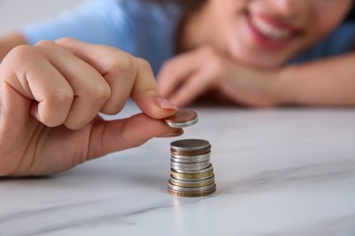 Photo of Young woman stacking coins at table, focus on hand. Money savings