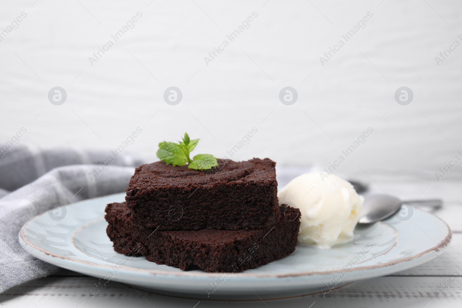 Photo of Tasty brownies served with ice cream and mint on white wooden table, closeup