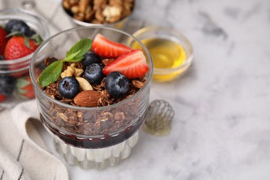 Photo of Tasty granola with berries, nuts, jam and yogurt in glass on white marble table, closeup. Space for text