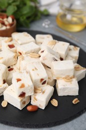 Photo of Pieces of delicious nutty nougat on black board, closeup
